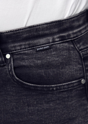 Detaljebillede af forlommen på den mørkegrå denim i farven Shadows – logo og snit fremhævet på plus-size model.