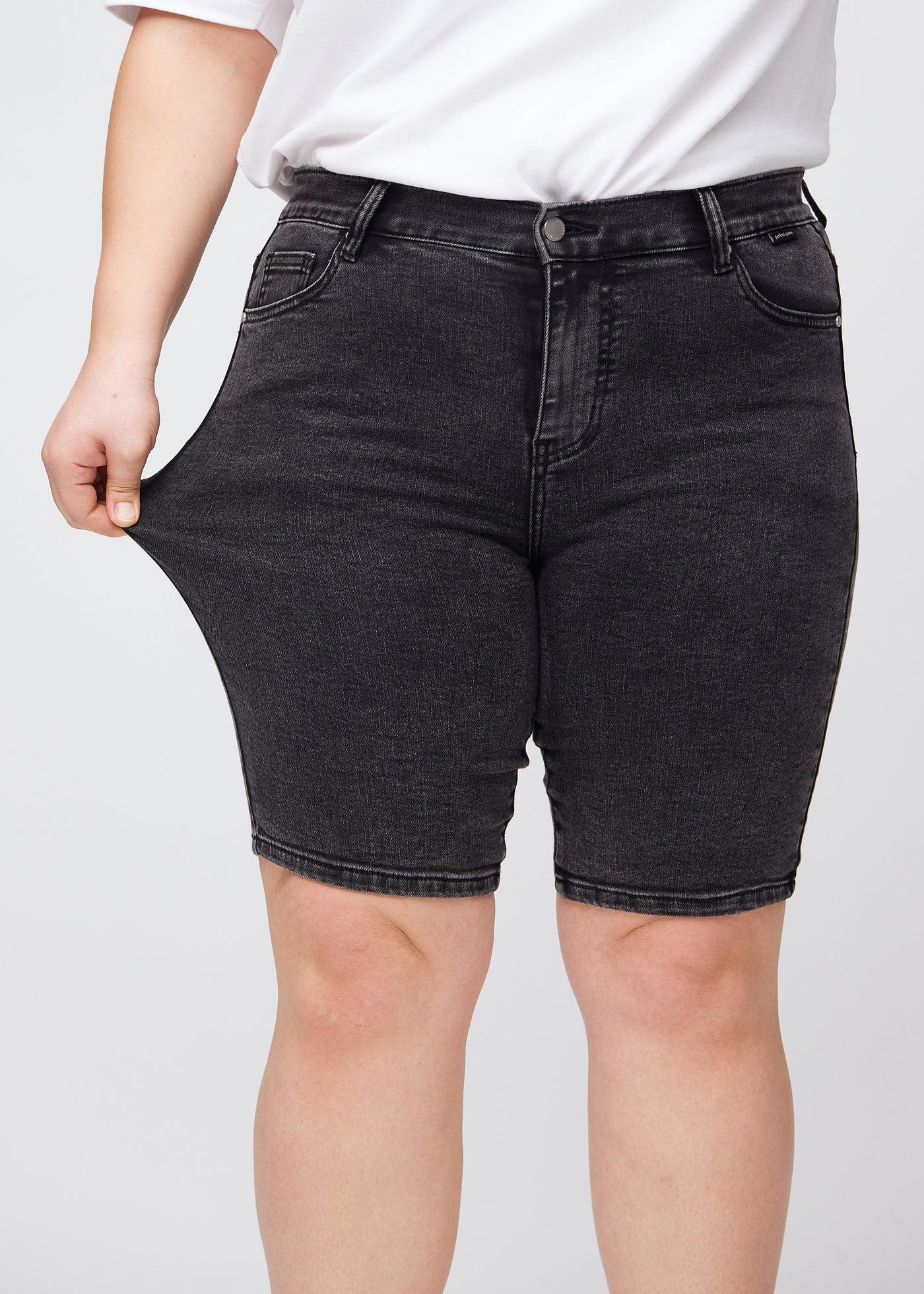 Plus-size model strækker shortsene ved låret for at vise stretch.