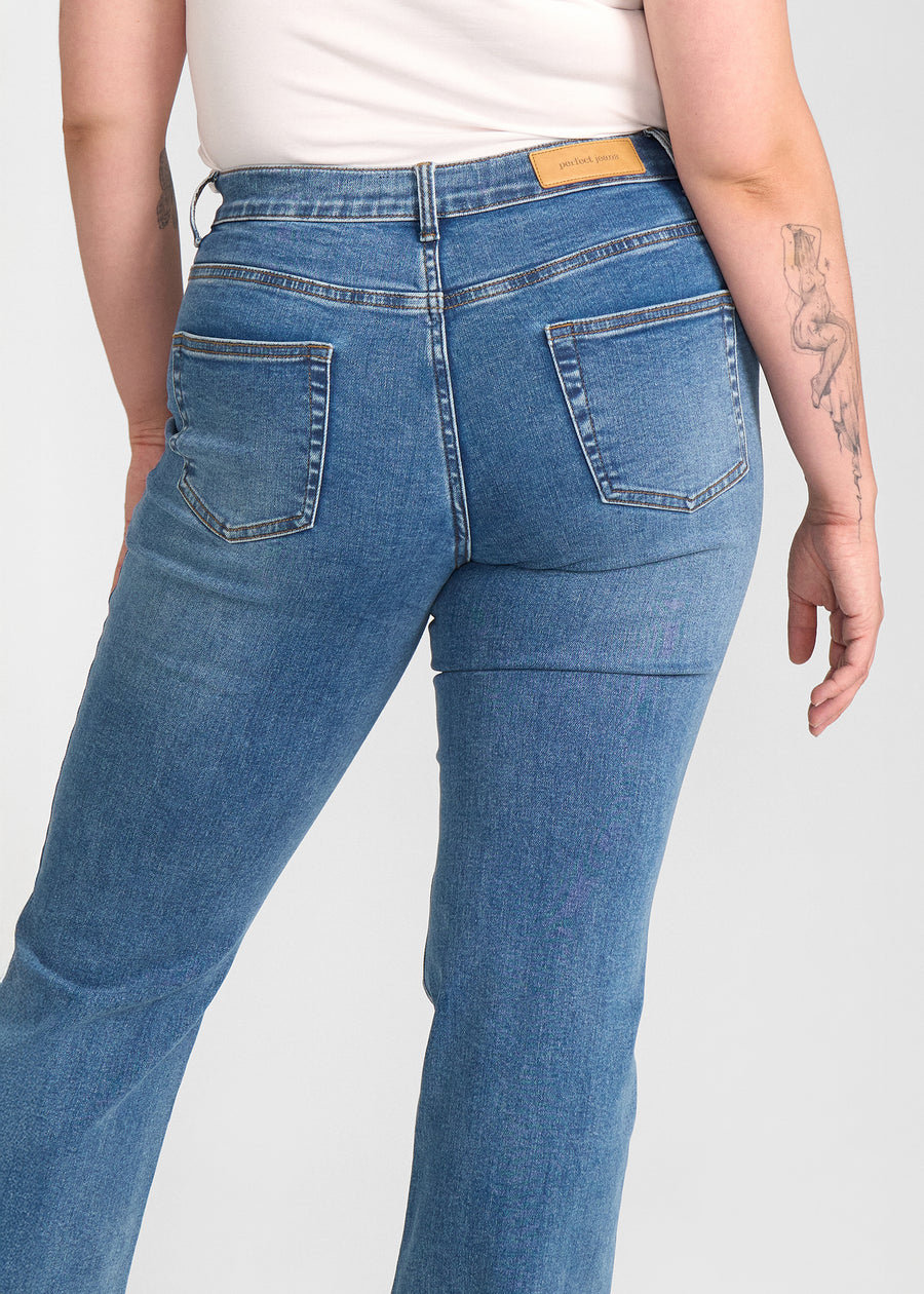 Blå denim bootcut jeans, modelnavn Rivers, som sidder tæt om hofter og lår med et let svaj fra knæet og ned, set bagfra tæt på for at vise detaljer. på en plus-size model.
