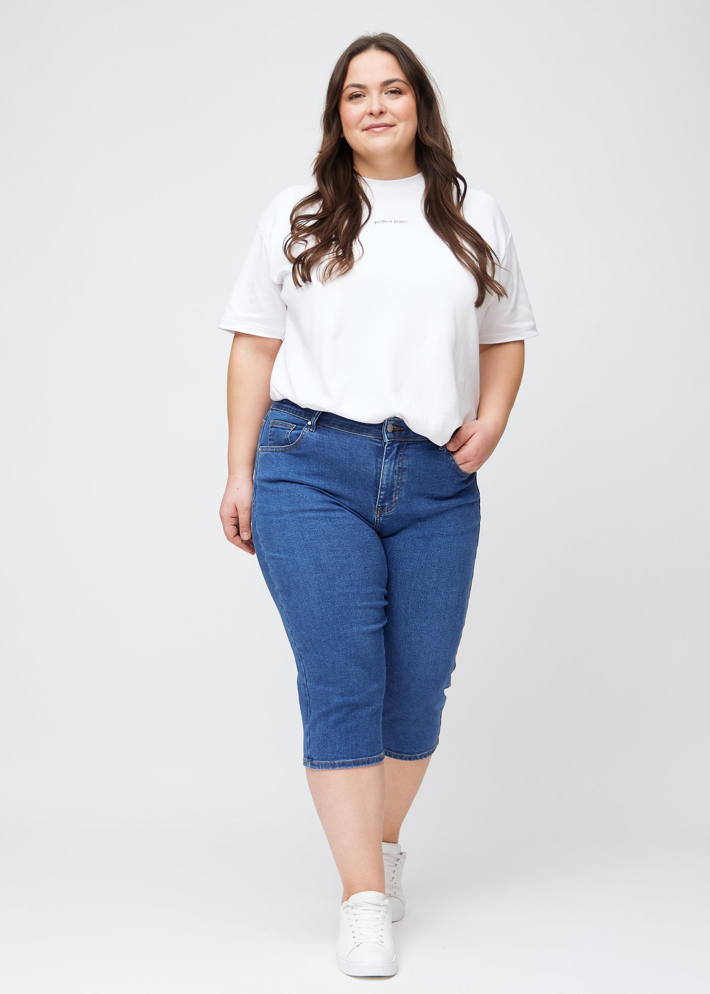 Plus-size model går ind i billedet, strækker i sine mørkeblå denim slim capris, drejer rundt for at vise dem frem og forlader derefter billedet.