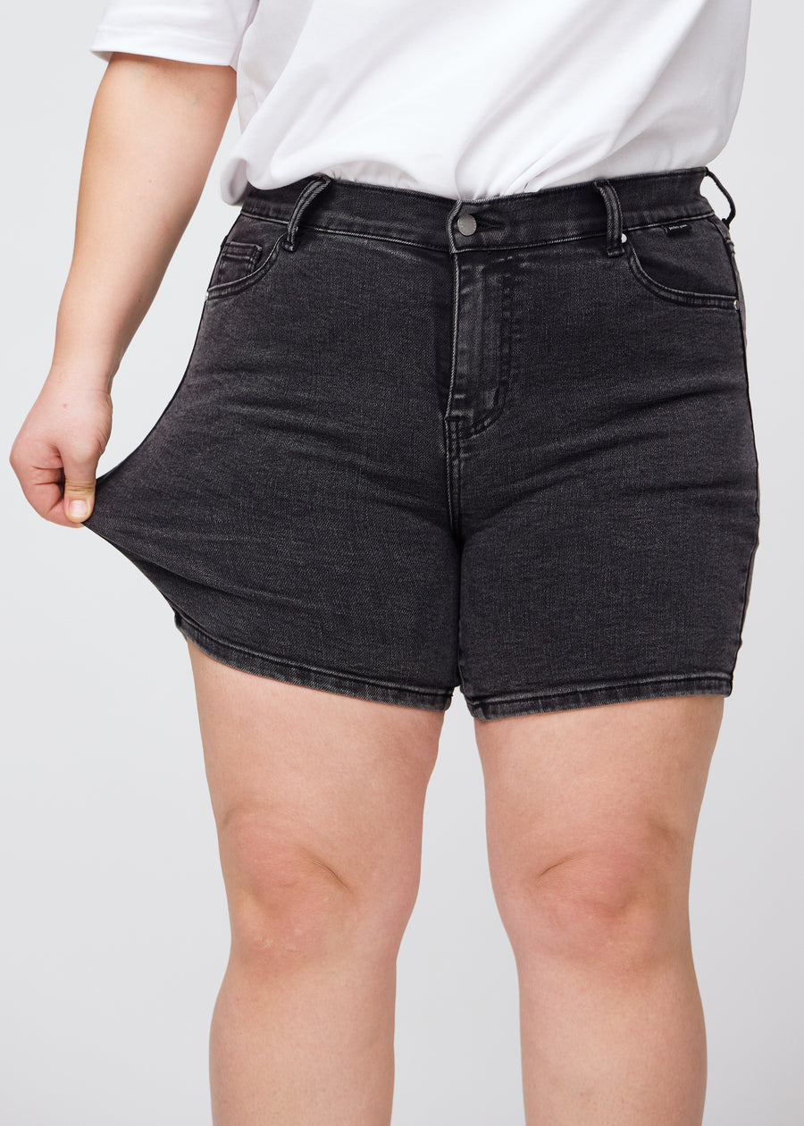 Plus-size model strækker shortsene ved låret for at vise stretch.