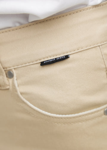 Close-up of beige jeans material with the Perfect Jeans logo label at the edge of the front pocket.