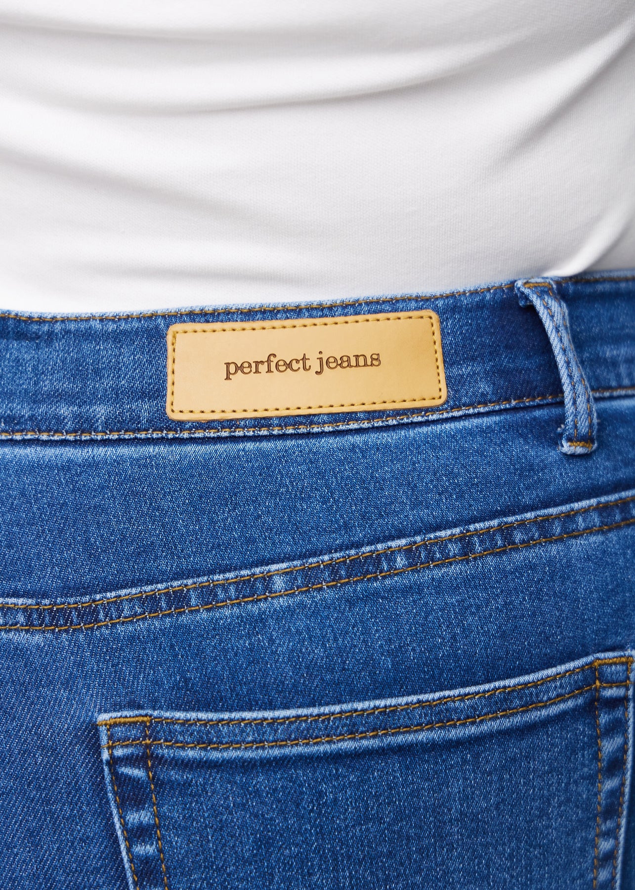 Close-up of dark blue denim with the Perfect Jeans leather patch at the back of the waistband on a plus-size model.