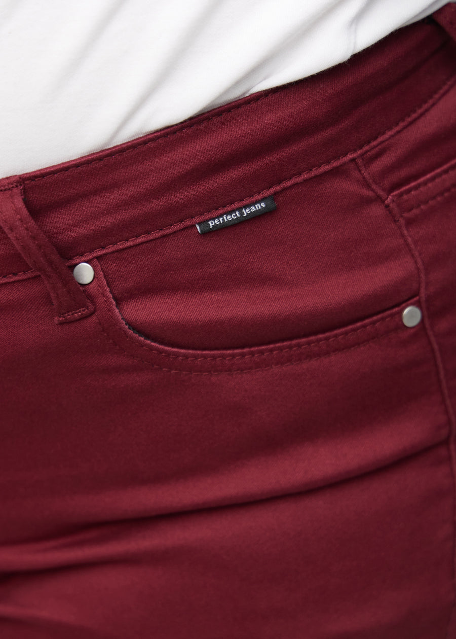 Nærbillede af rødt jeansmateriale med Perfect Jeans logoetiket ved forlommekanten, på en plus-size model.