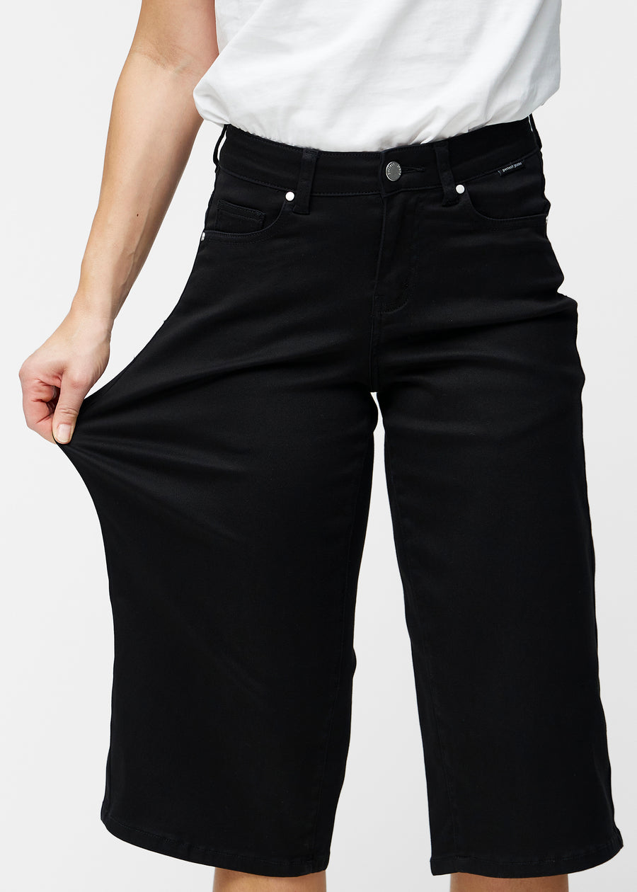 Model strækker de løse, sorte capris i farven Ravens ved hoften for at vise materialets stretch.