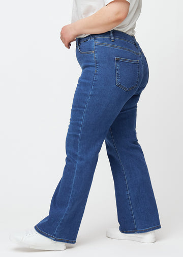 Dark blue mid-rise bootcut jeans in Oceans. Side view on a plus-size model.