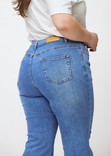 Blue mid-rise bootcut jeans in Rivers. Close-up back view on a plus-size model, showing the details.