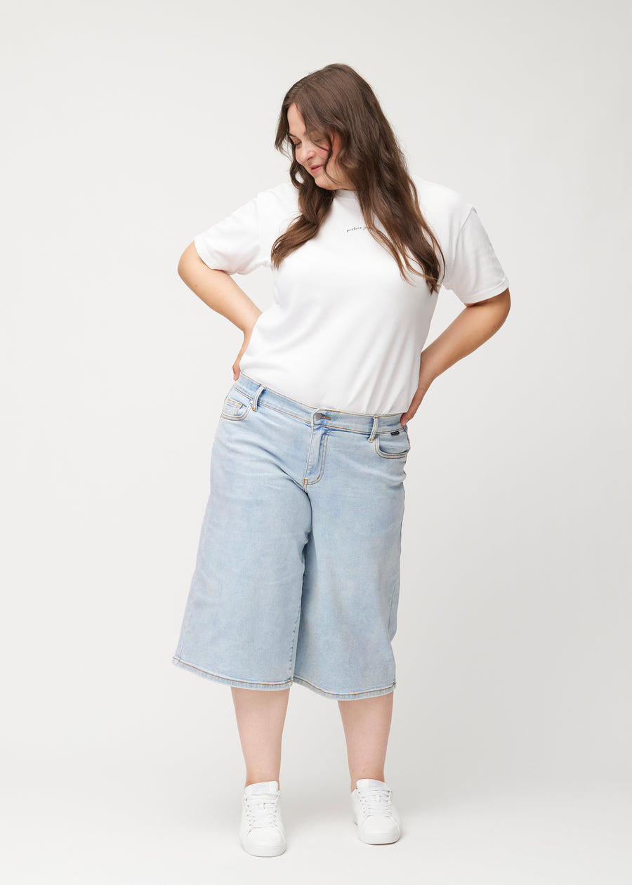 Full-length view of a plus-size model wearing loose, light blue Waves denim capris that end just below the knee.