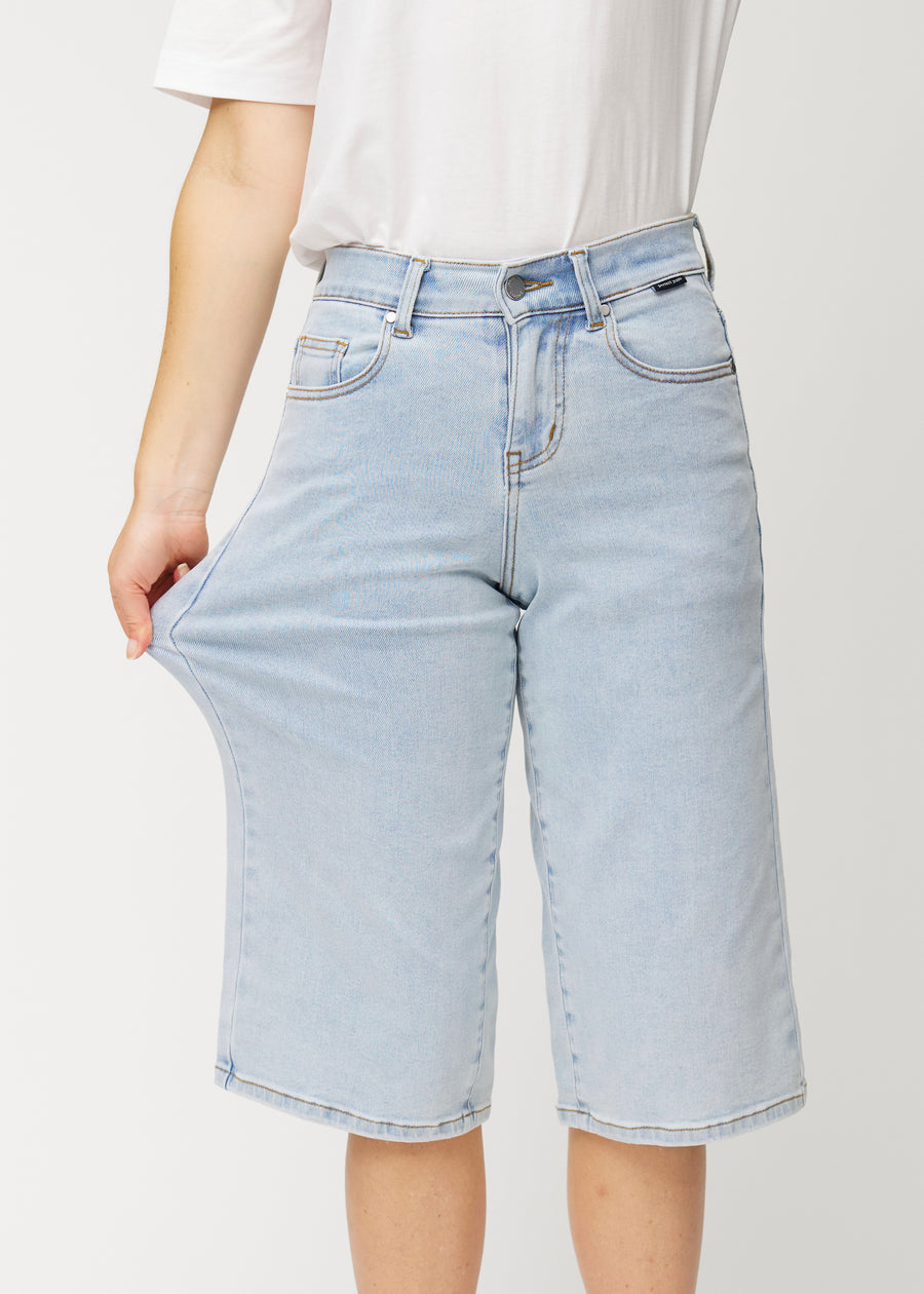 Model stretches the loose, light blue Waves denim capris at the hip to show the fabric&