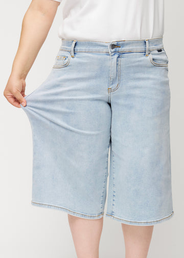 Plus-size model stretches the loose, light blue Waves denim capris at the hip to show the fabric&