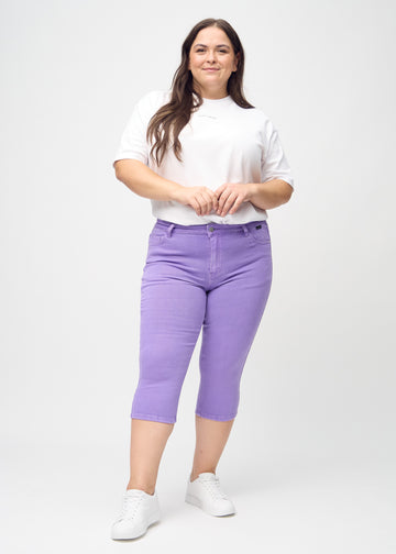 Skinny capris for women in pastel purple fabric, color Lavenders. Full-length view of a plus-size model wearing the capris.