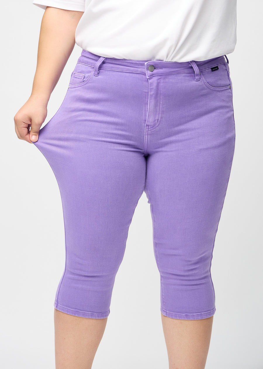 Skinny capris for women in pastel purple fabric, color Lavenders. A plus-size model stretches the fabric to demonstrate its flexibility.