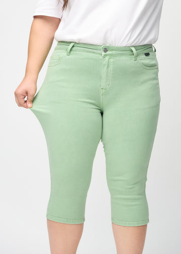 Skinny capris for women in pastel green fabric, color Mints. A plus-size model stretches the fabric to demonstrate its flexibility.