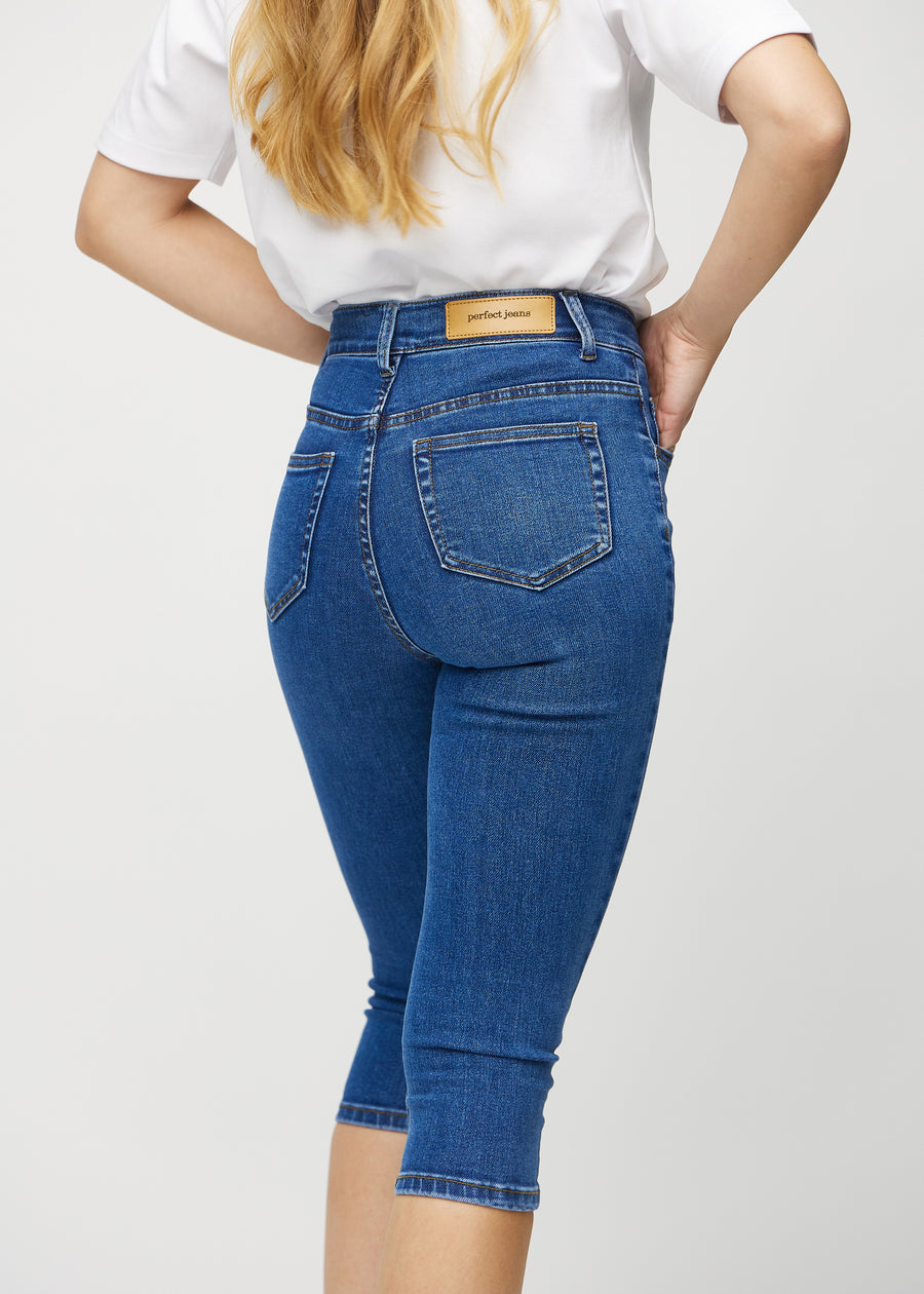 Skinny capris for women in dark blue denim, color Oceans. Close-up from behind on a model, highlighting pockets and stitching.