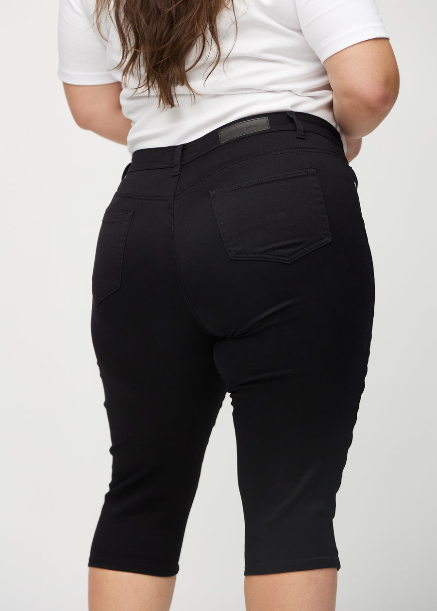 Skinny capris for women in black fabric, color Ravens. Close-up from behind on a plus-size model, highlighting pockets and stitching.