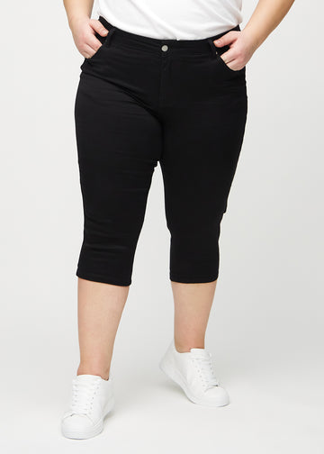 Skinny capris for women in black fabric, color Ravens. Front view on a plus-size model, showing the close-fitting legs ending just below the knee.