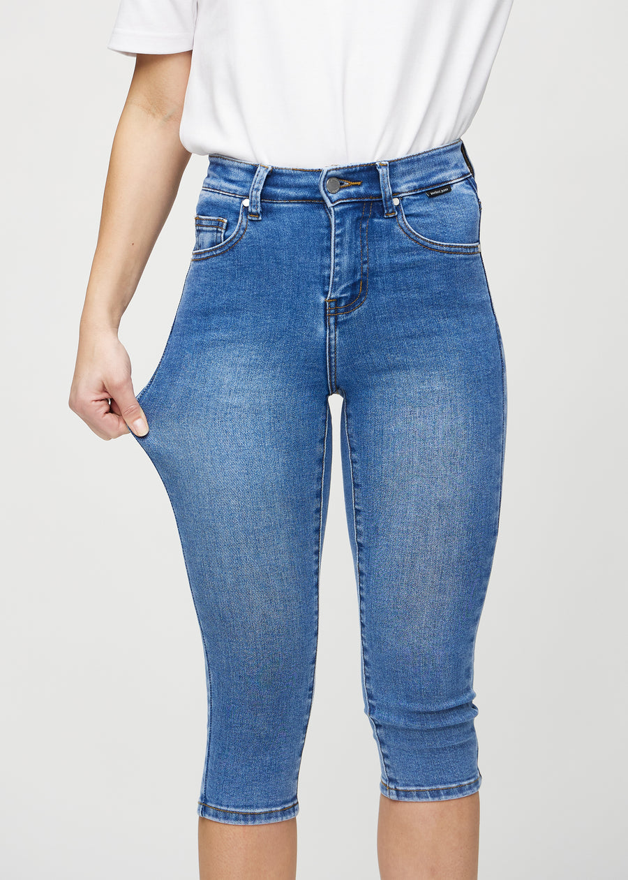 Skinny capris for women in blue denim, color Rivers. A model stretches the fabric to demonstrate its flexibility.