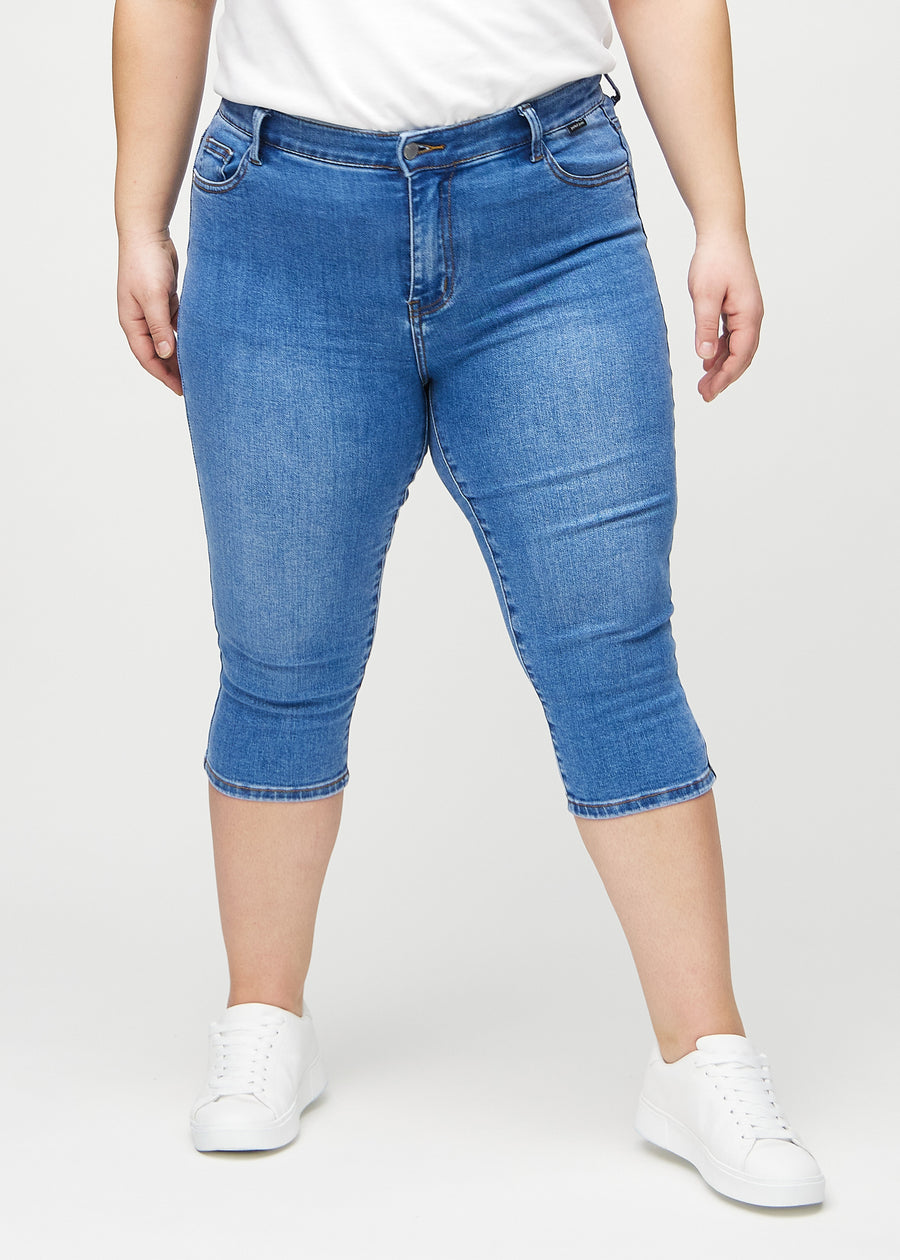 Skinny capris for women in blue denim, color Rivers. Front view on a plus-size model, showing the close-fitting legs ending just below the knee.