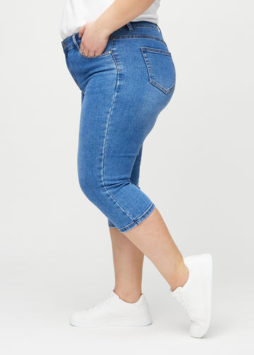 Skinny capris for women in blue denim, color Rivers. Side view on a plus-size model, showing the fitted cut.