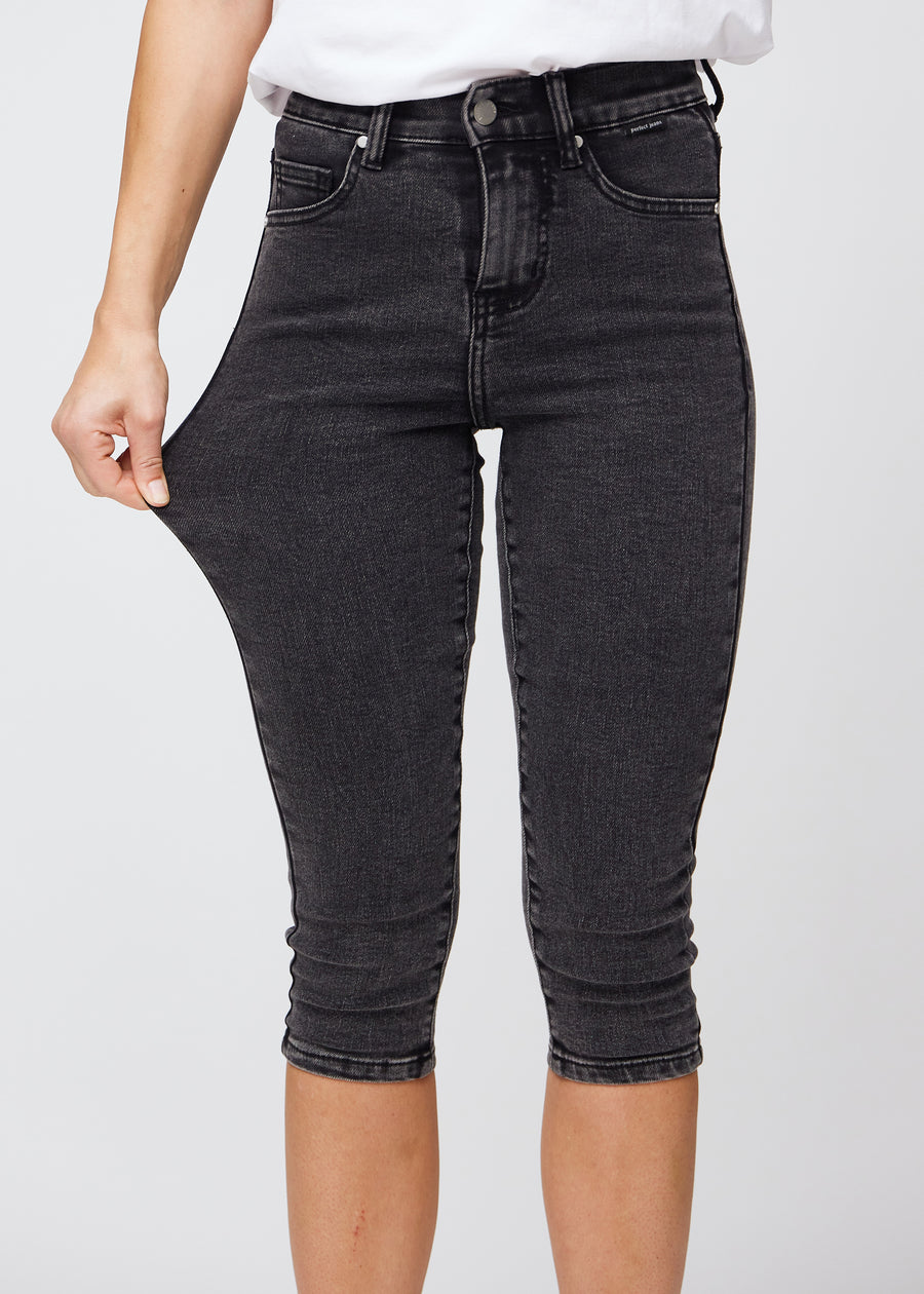 Skinny capris for women in dark grey denim, color Shadows. A model stretches the fabric to demonstrate its flexibility.