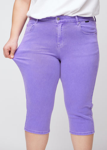 Slim capris for women in pastel purple jeans fabric, color Lavenders. A plus-size model pulls the fabric at the thigh to demonstrate stretch and flexibility.
