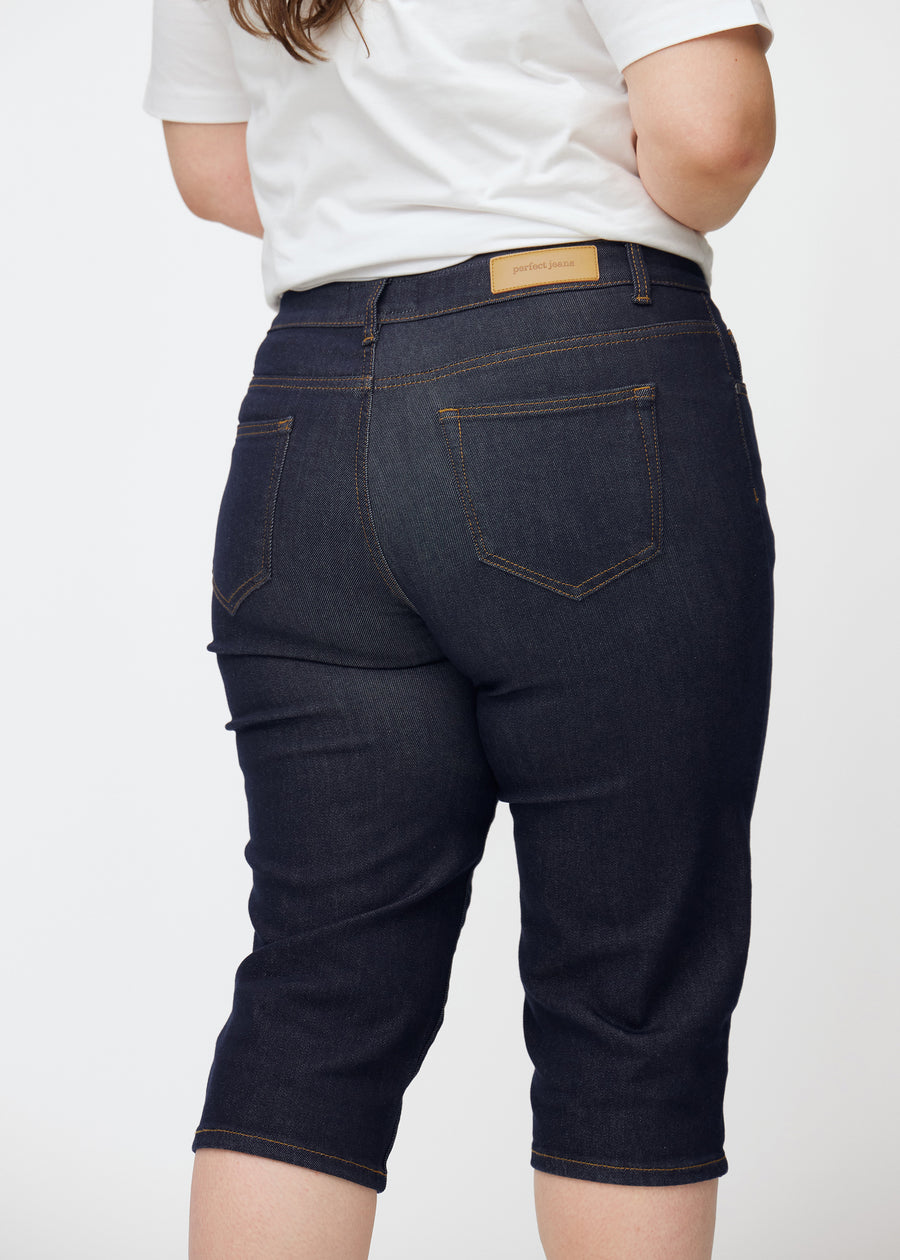 Deep dark blue denim capris for women in the colour Midnights seen from the back in close-up on a plus-size model.