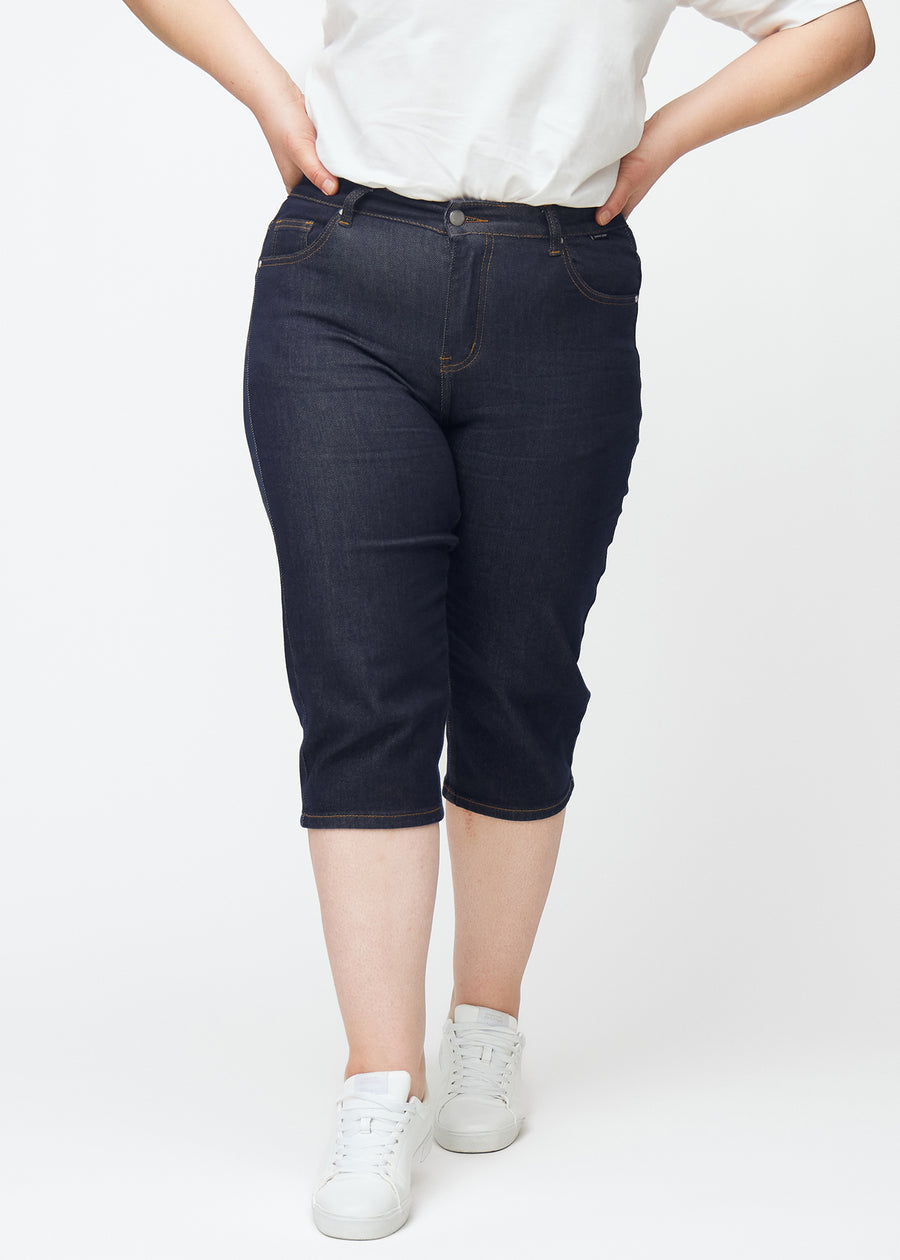 Deep dark blue denim capris for women in the colour Midnights with a slim fit seen from the front on a plus-size model.