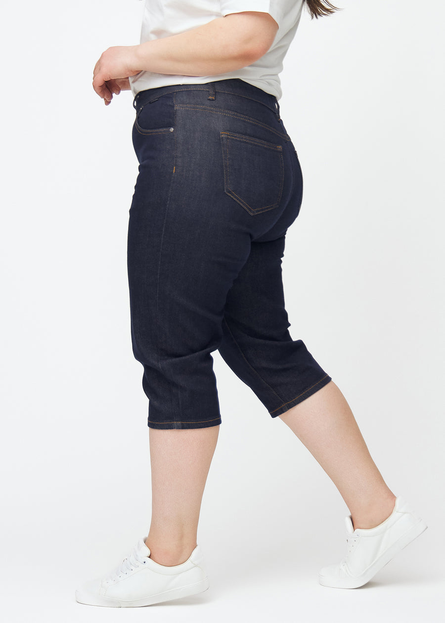 Deep dark blue denim capris for women in the colour Midnights with a slim fit seen from the side on a plus-size model.