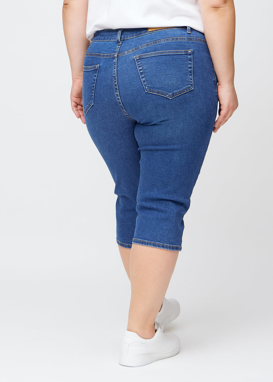 Slim capris for women in dark blue denim, color Oceans. Back view on a plus-size model, showing the fit, length and back pockets.