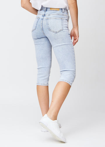 Slim capris for women in light blue denim, color Waves. Back view on a model, showing the fit, length and back pockets.