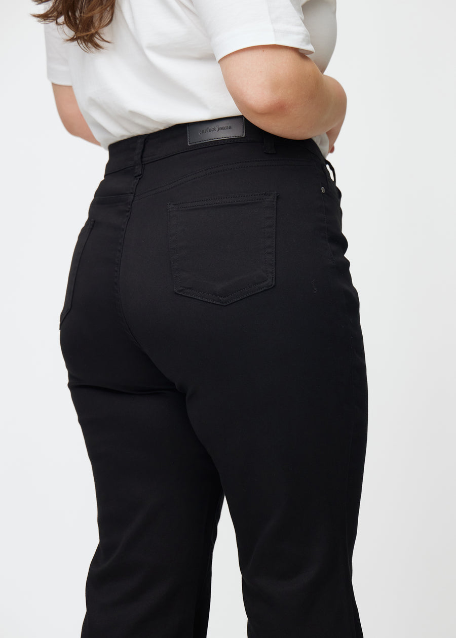Black high-waisted bootcut jeans seen from the back up close on a plus-size model to show details.