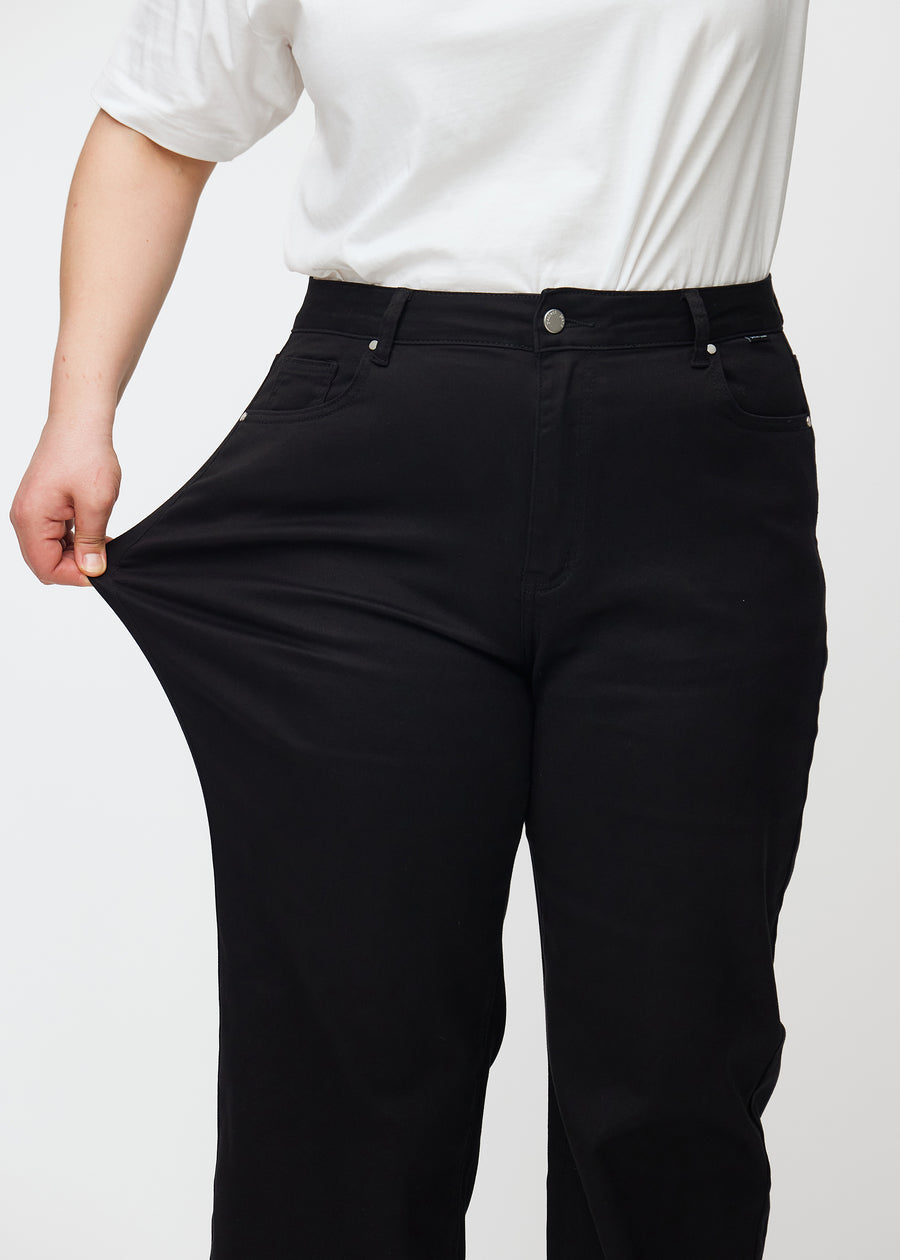 The plus-size model stretches the jeans at the thigh to show the stretch.