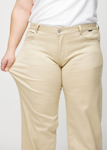 Loose jeans for women in beige, color Gazelles. A plus-size model stretches the denim at the thigh to show the fabric&