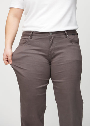 The plus-size model stretches the jeans at the thigh to show the stretch.