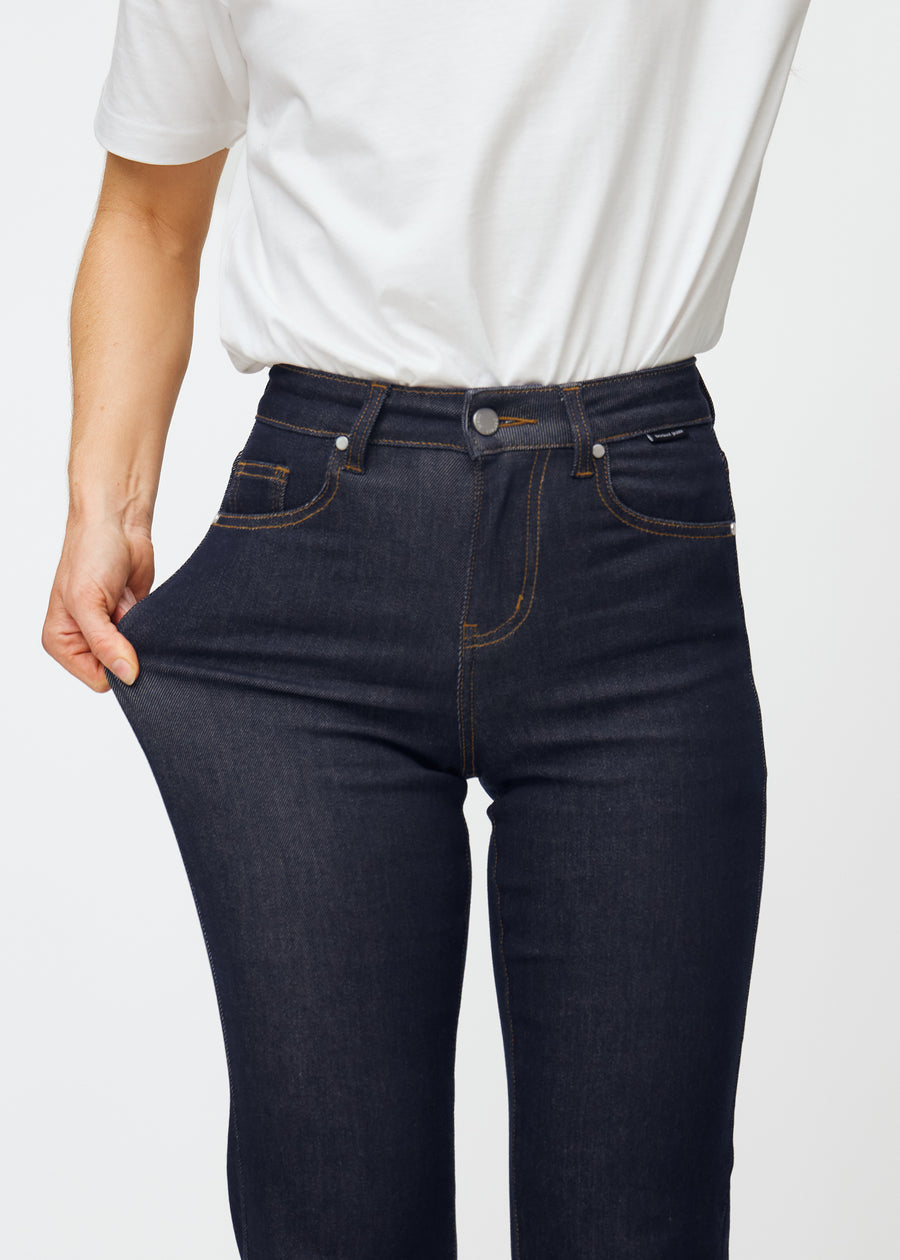 The model stretches the deep dark blue denim jeans for women in the color Midnights at the thigh to show the material&