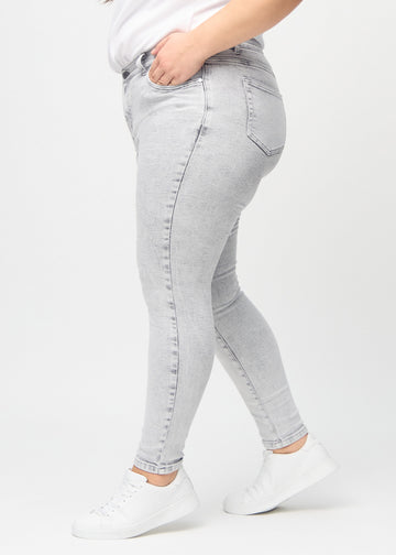 Light grey denim skinny jeans seen from the side on a plus-size model.