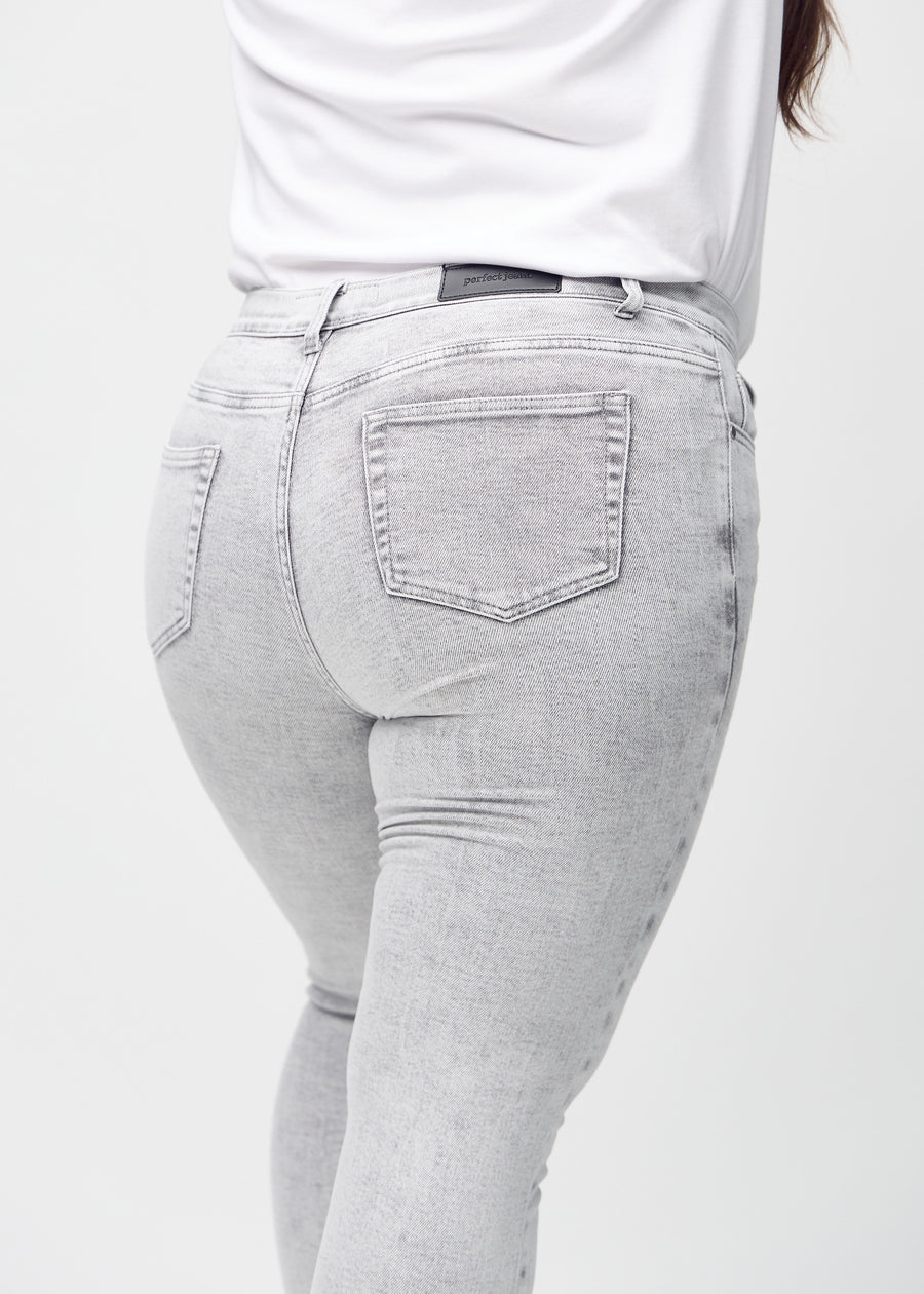 Light grey denim skinny jeans seen from the back close up on a plus-size model to show details.