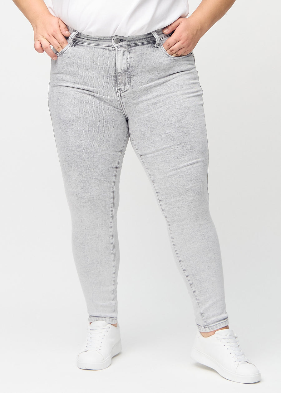 Light grey denim skinny jeans, model name Ashes, which fits tightly along the leg on a plus-size model, seen from the front.