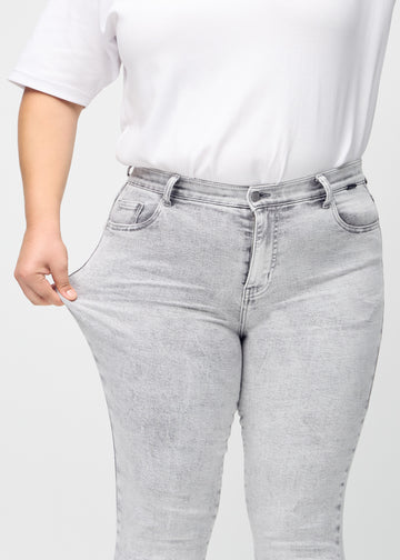 A plus-size model stretches the jeans at the thigh to show the stretch