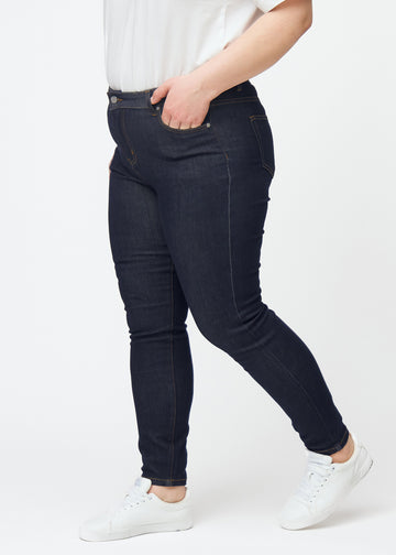 Deep dark blue denim jeans for women in the color Midnights with a skinny fit, viewed from the side on a plus-size model.