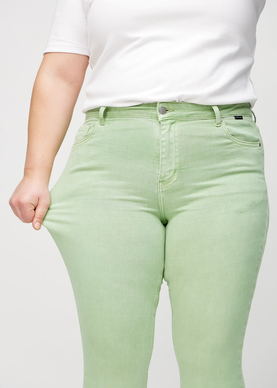 Skinny jeans for women in light green, color Mints. A plus-size model stretches the jeans at the thigh to show the fabric&