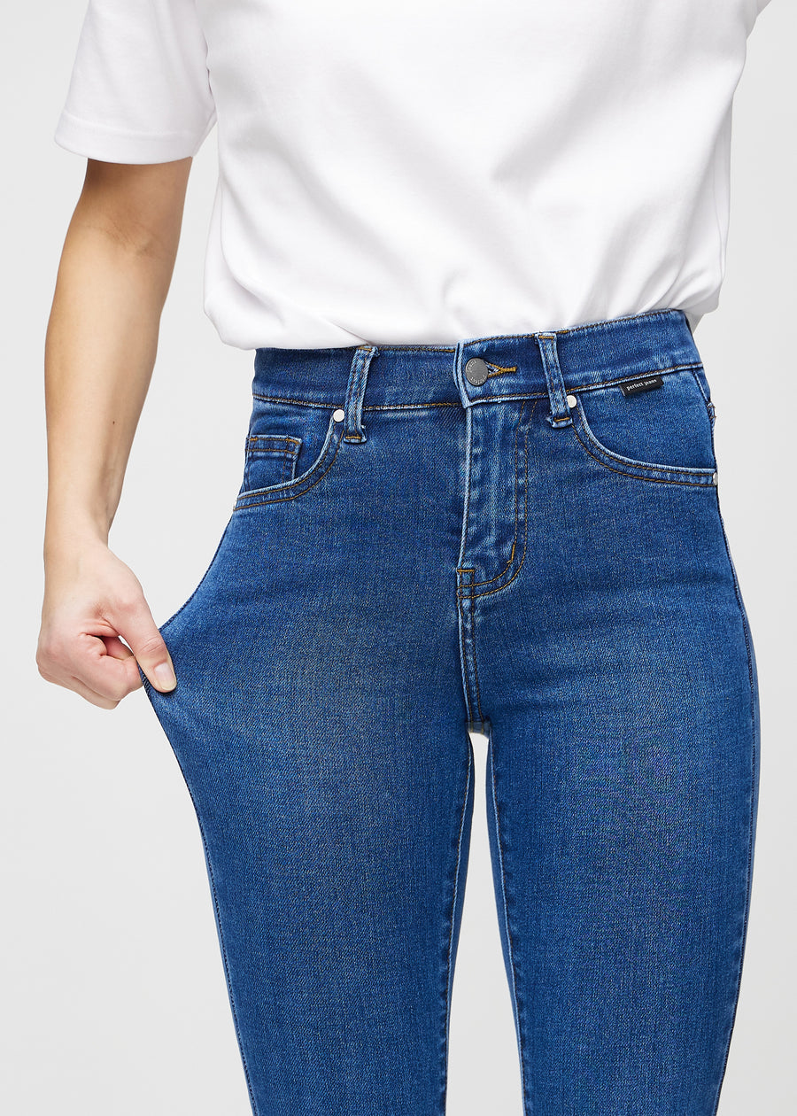 Skinny jeans for women in dark blue, color Oceans. A model stretches the jeans at the thigh to show the fabric&