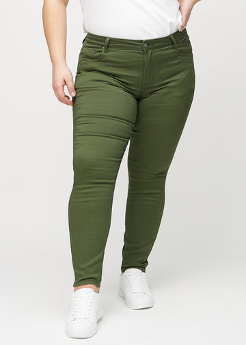 Dark green skinny jeans, model name Renewals, which fit tightly on the leg on a plus-size model, seen from the front.