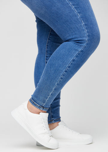 Skinny jeans for women in blue, color Rivers. Close-up of the snug-fitting leg openings at the ankles on a plus-size model.