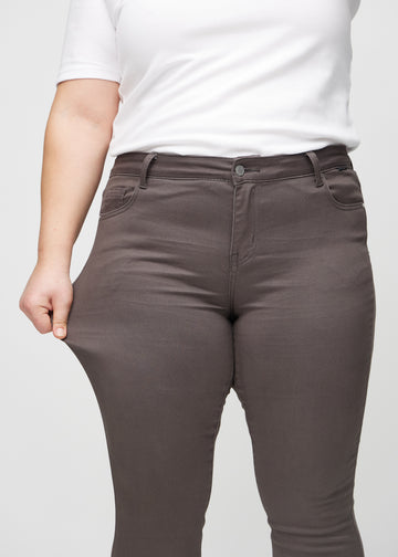 The plus-size model stretches the jeans at the thigh to show the stretch.