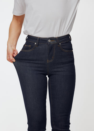 The model stretches the deep dark blue denim jeans for women in the color Midnights at the thigh to show the material&