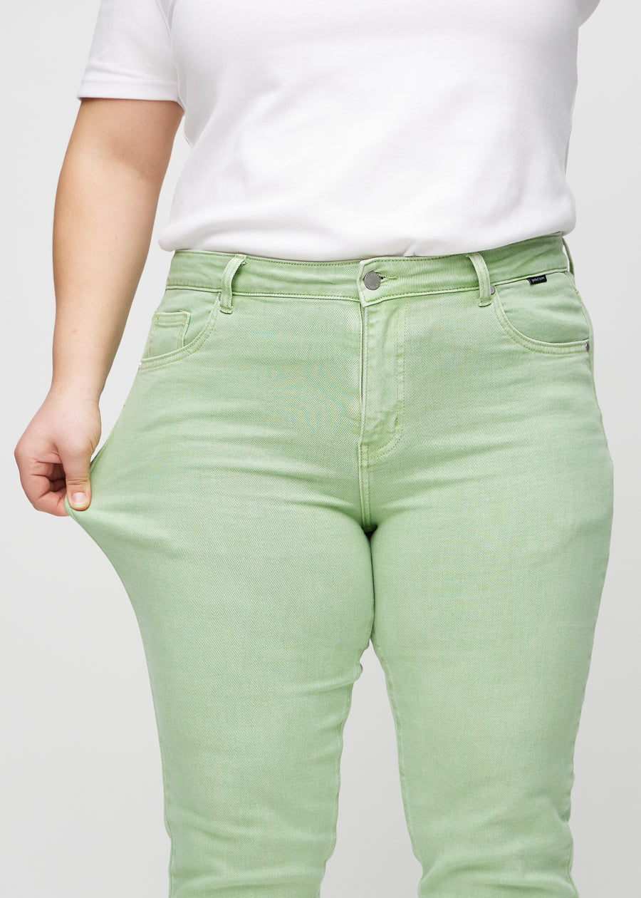Slim jeans for women in light green, color Mints. A plus-size model stretches the jeans at the thigh to show the fabric&