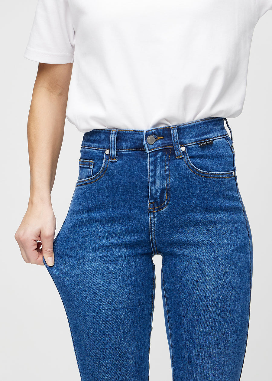 Slim jeans for women in dark blue, color Oceans. A model stretches the jeans at the thigh to show the fabric&