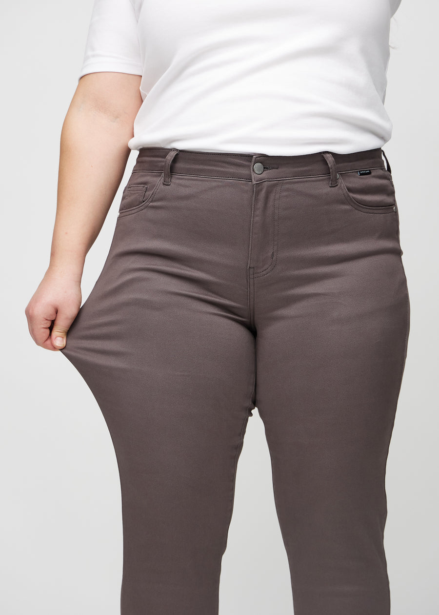Slim jeans for women in grey-brown, color Thunders. A plus-size model stretches the jeans at the thigh to show the fabric&