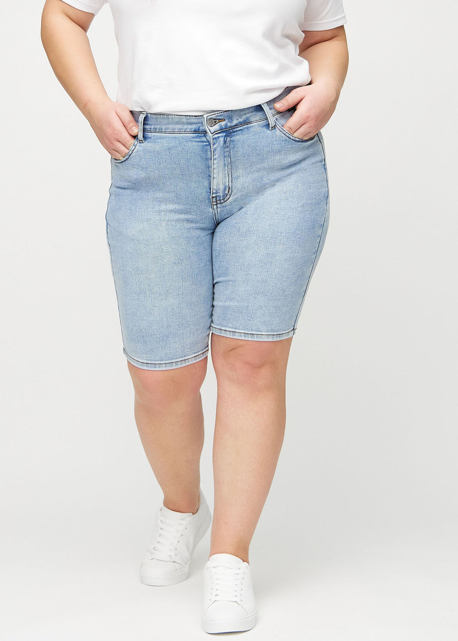 Light denim skinny middle shorts, model name Waves, which fit tightly around the thigh and end just above the knee on a plus-size model, seen from the front.